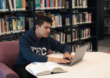 Indian student studying with a laptop and textbooks in a library while preparing to study abroad without IELTS